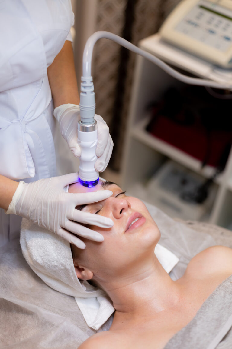 A young beautiful girl lies on the beautician's table and receives procedures with a professional apparatus for skin rejuvenation and moisturizing